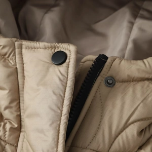 Macro shot of khaki quilted jacket with matte black snap buttons and zipper detail