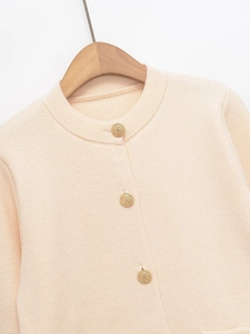 Close-up of beige knit cardigan featuring embossed gold buttons and ribbed neckline