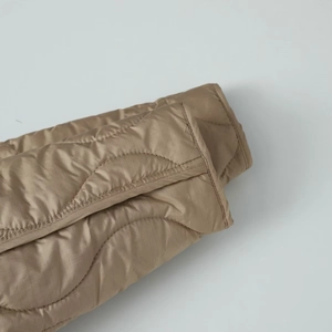 Detailed view of champagne gold quilted jacket sleeve with wave stitching and fine texture