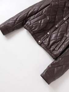 Detailed view of quilted faux leather jacket texture with snap buttons and elastic cuffs