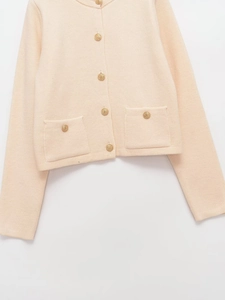 Detail view of apricot knit cardigan featuring textured gold buttons and pocket accents