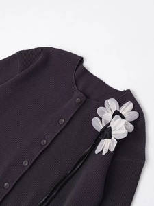 Detail der Strickjacke mit großen weißen Organzablumen und schwarzen Bandquasten