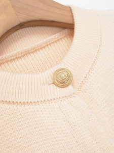 Detailed close-up of ribbed crewneck and golden vintage button on beige knit cardigan