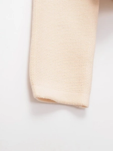 Macro shot of fine-knit cream cardigan sleeves showing soft texture and ribbed cuff detail