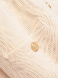 Detail view of knit cardigan with embossed gold buttons and flat patch pocket texture