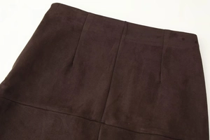 Detail of dark brown suede skirt showing vertical seams and matte fabric texture