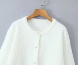 Détail d'un cardigan blanc en maille pelucheuse avec col rond et boutons perlés