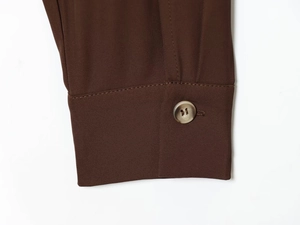Détail d'une manche de chemise marron foncé avec bouton marbré et texture de tissu premium