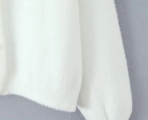 Gros plan détaillé sur la texture pelucheuse blanche et le bouton perle du cardigan doux