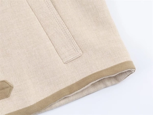 Detailed close-up of beige woven jacket fabric with contrast brown binding and stitching