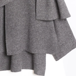 Détail du tissu en maille gris foncé avec volants superposés et texture douce du manteau