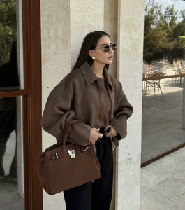 Detail view of a cropped dark brown woolen jacket with classic suede leather handbag