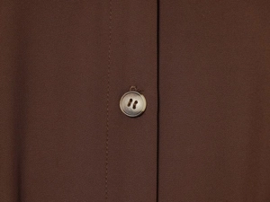 Gros plan sur un bouton marbré et les plis d'une chemise pour femme couleur marron