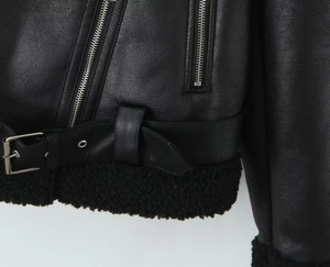 Detail of black faux leather motorcycle jacket with warm shearling lining and belt buckle