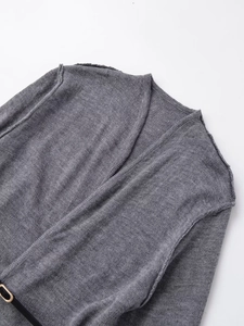 Dettaglio di un cardigan grigio in maglia con scollo a V, trama tessuta e cintura