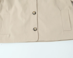 Close-up of the beige trench coat's lapel with tortoise buttons and vertical pockets