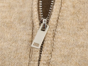Macro view of silver rectangular metal zipper and soft beige chunky knit texture