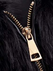 Close-up of premium gold metal zipper on a black faux fur jacket with leather trim