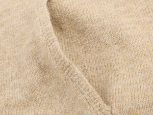 Macro view of oatmeal knitted hoodie fabric showing fine stitch texture and seam detail