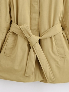 Detalle de gabardina caqui con cinturón anudado y bolsillos laterales simétricos