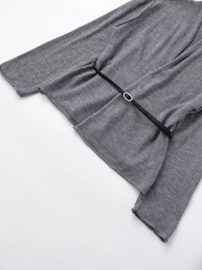 Dettaglio del top in maglia grigia con trama fine e sottile cintura nera con fibbia dorata
