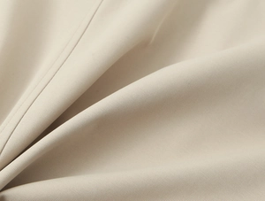 Close-up of beige trench coat fabric texture showing fine twill and premium stitching detail