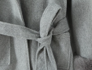 Detail of waist tie and wool texture on a grey hooded cloak coat with fur cuffs