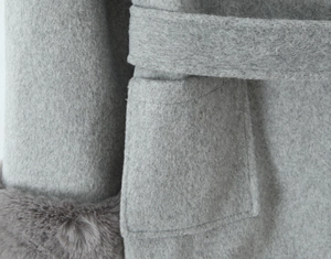 Detail of grey wool coat featuring side pockets, waist tie belt and faux fur sleeve cuffs