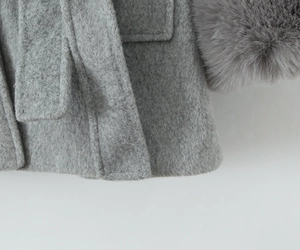 Detailed view of grey wool coat featuring faux fur cuffs and a decorative pocket