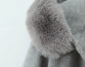 Close-up of grey hooded cloak coat featuring plush faux fox fur trim and textured wool fabric