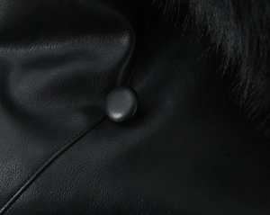 Close-up of black PU leather jacket with faux fur trim and textured leather button