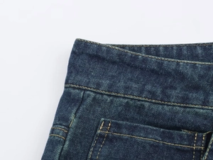 Detalle de los vaqueros azul oscuro que muestra la textura sarga y costuras naranjas