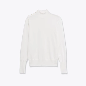 Detailed view of gold buttons on shoulder and ribbed cuffs of white knit sweater
