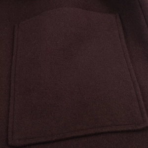 Detail of the stitched patch pocket on a dark burgundy wool coat with fine texture