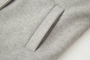Détail de la poche passepoilée et de la texture du tissu sur ce manteau en laine gris clair