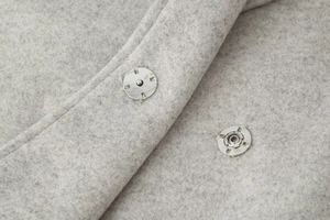 Détail des boutons-pression en métal argenté sur le tissu en laine gris clair du manteau