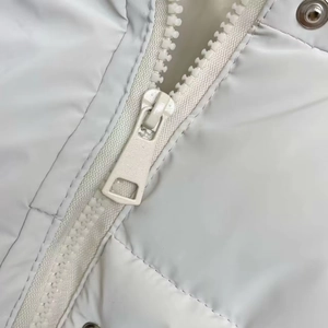 Close-up of cream white quilted puffer vest featuring resin zipper and metal snap buttons