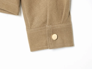 Detail of khaki twill fabric sleeve with a polished gold metal button on the cuff