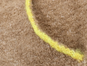 Gros plan sur tissu tricoté marron avec détails de surpiqûres jaune fluo contrastées