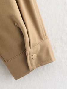 Detail of khaki twill jacket sleeve featuring a polished gold metal snap button