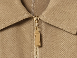 Close-up of golden zipper on khaki jacket featuring premium twill fabric texture