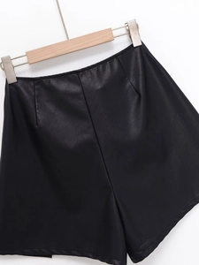 Detailed view of black PU leather skirt shorts with pleated waist on a wooden hanger