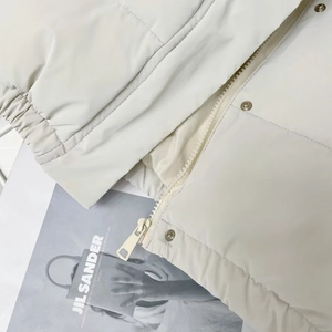 Detail of cream PU leather vest showing zipper, metal snap buttons and elastic hem