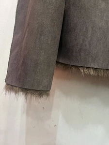 Detailed close-up of dark taupe suede jacket with brown faux fur lining and stitched hems