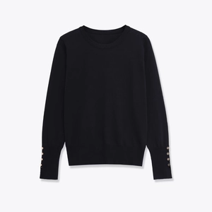 Close-up of black knitted sweater showing gold metal buttons on ribbed cuffs