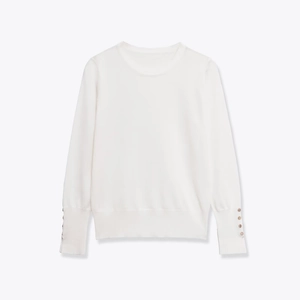 Detailed close-up of white knit top featuring elegant golden buttons on ribbed cuffs