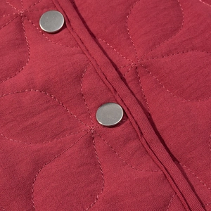 Macro shot of dark red quilted jacket fabric with metal snap button and petal stitching