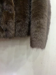 Detail view of coffee faux fur texture with black round resin button on winter jacket