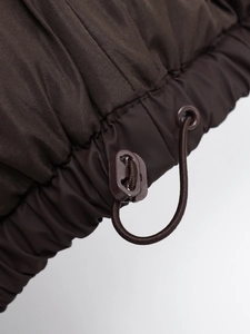 Detailed view of adjustable drawstring hem with plastic toggles on dark brown puffer vest