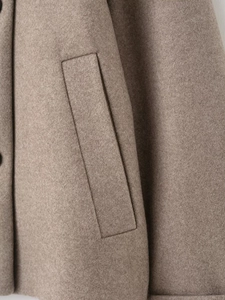 Macro detail of oat-colored wool jacket featuring a side welt pocket and button craftsmanship
